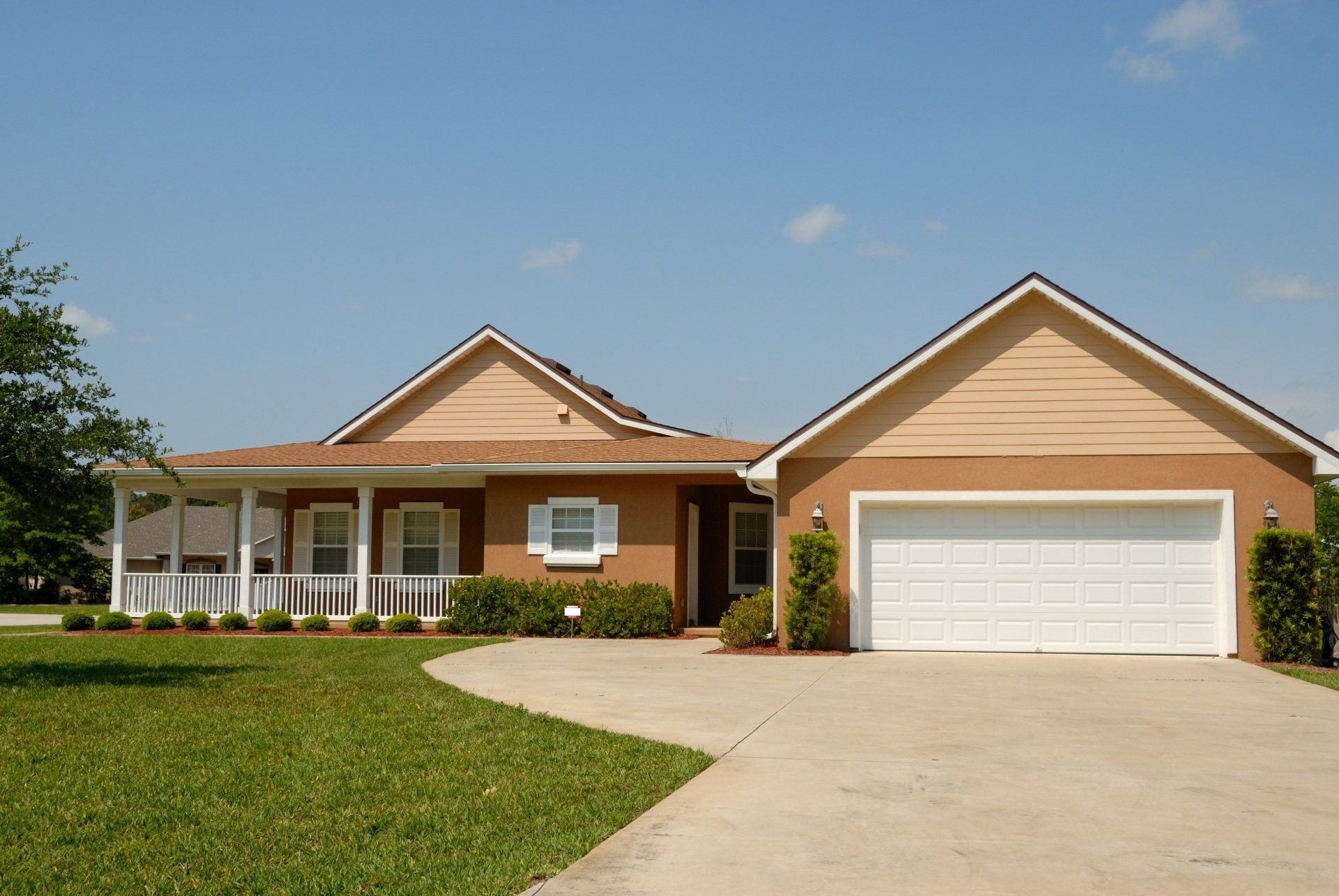 Single-story suburban house with beige siding, a white garage door, and a curved driveway under a blue sky